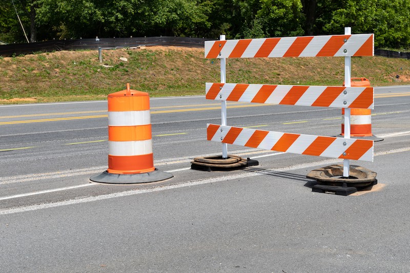 Traffic safety barricade and barrels with orange and white stripes on an asphalt street, horizontal aspectalt