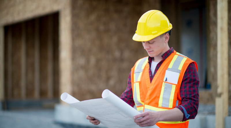 construction worker in yellow hard hat looking over traffic plans